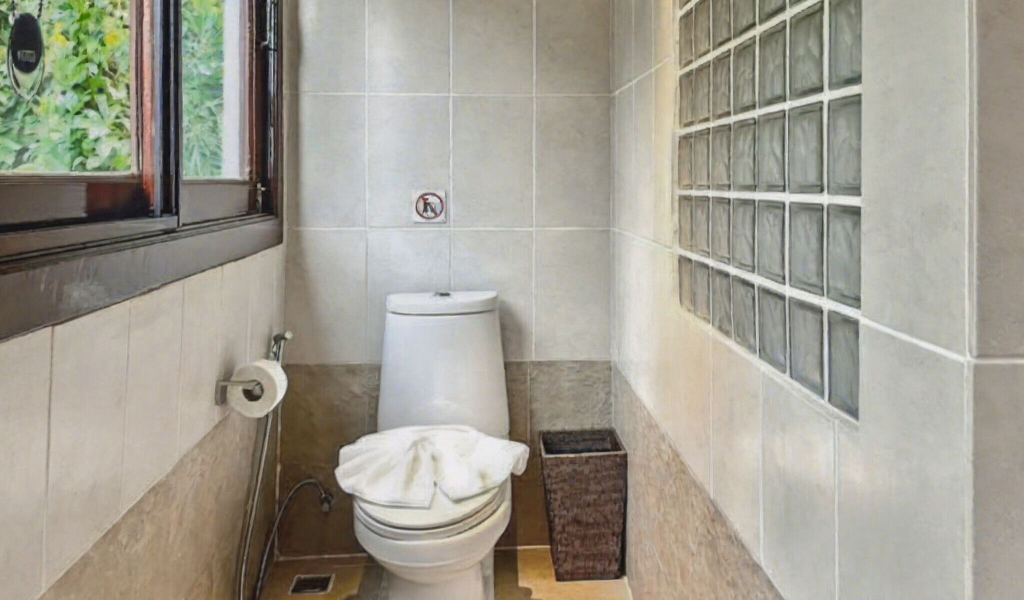 A small bathroom with a toilet, a window, and a tiled wall.