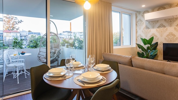 Un comedor con una mesa redonda dispuesta para cuatro personas, un sofá y un televisor en la pared.