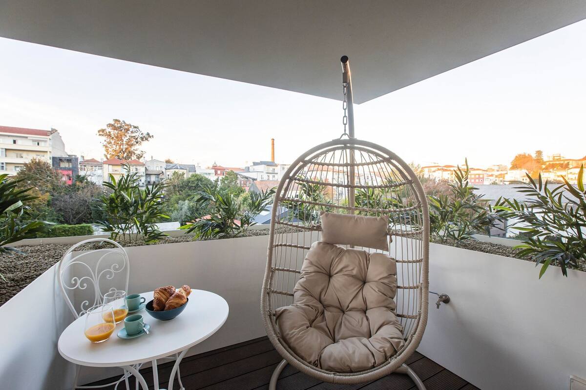 A balcony with a hanging chair, a small table with a bowl of croissants, and a cup of coffee.