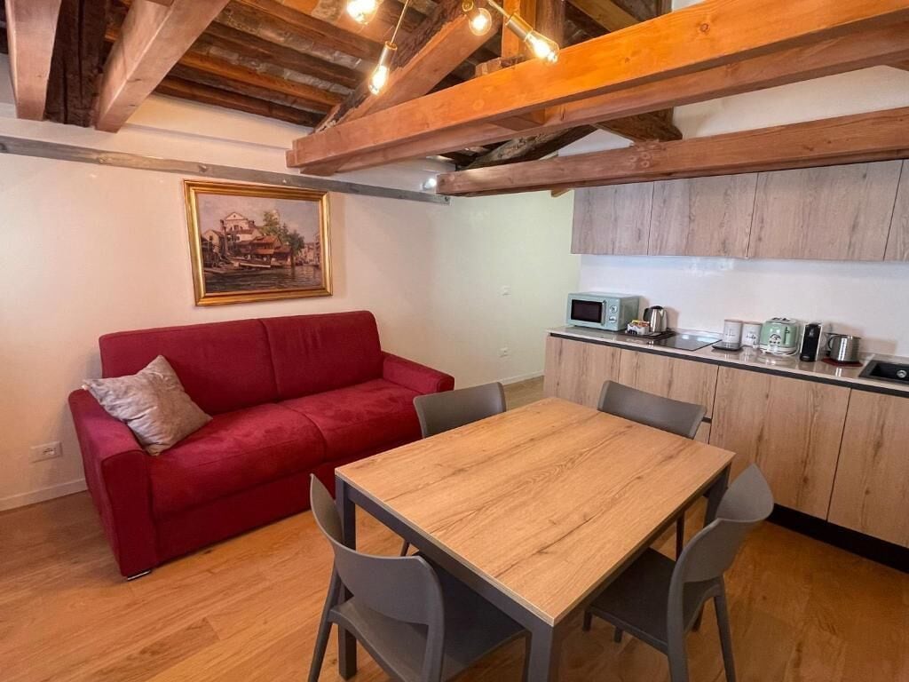 A cozy living area with a red sofa, a wooden dining table, and a kitchen with wooden cabinets and appliances.