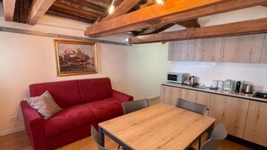 Uma sala de estar acolhedora, com um sofá vermelho, uma mesa de jantar de madeira e uma cozinha com armários e eletrodomésticos de madeira.