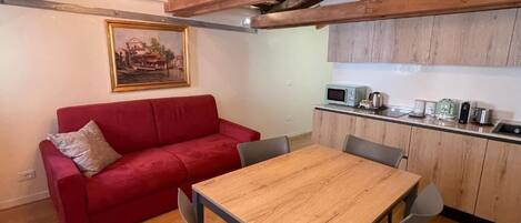 A cozy living area with a red sofa, a wooden dining table, and a kitchen with wooden cabinets and appliances.