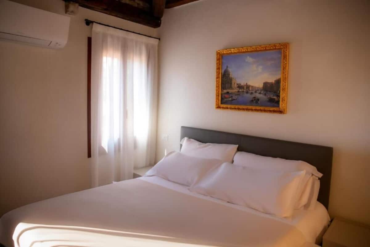 Quarto de hotel com cama bem arrumada, pintura de paisagem urbana na parede e janela com cortinas.