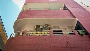 Un immeuble à plusieurs étages, doté d’une façade en briques rouges, de climatiseurs et d’un balcon avec des garde-corps jaunes.
