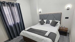 A modern bedroom with a bed, curtains, a nightstand, and a wall-mounted air conditioner. - The Shivaay Palace (Varanasi)