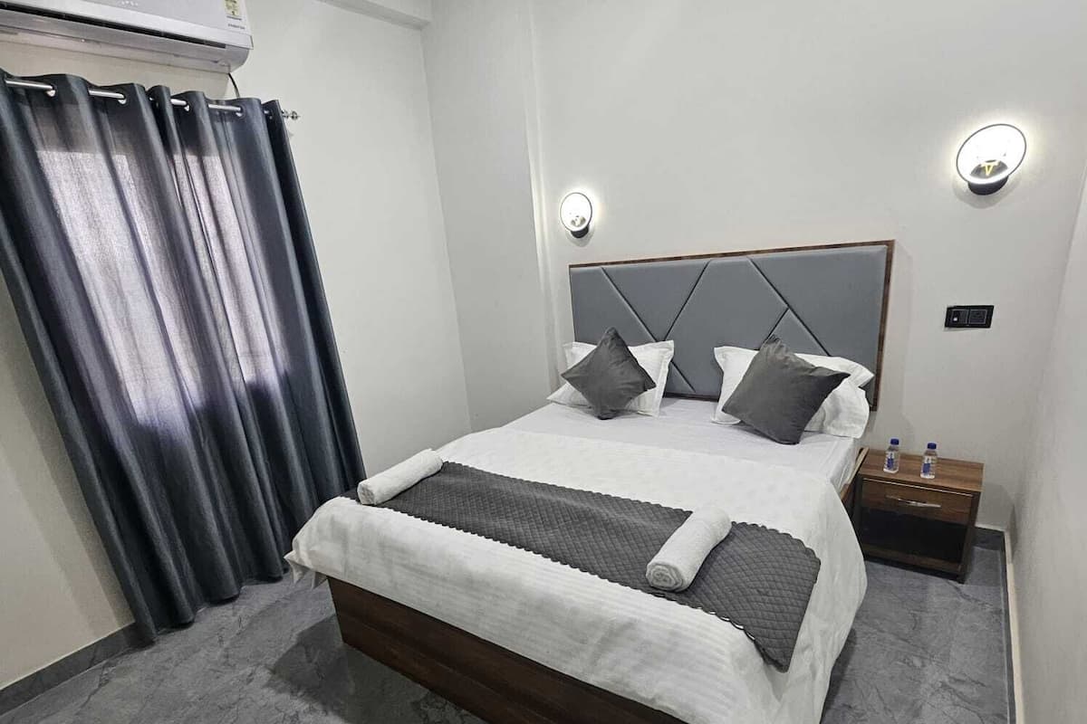 Un dormitorio moderno con una cama, cortinas, una mesita de noche y un aire acondicionado instalado en la pared.