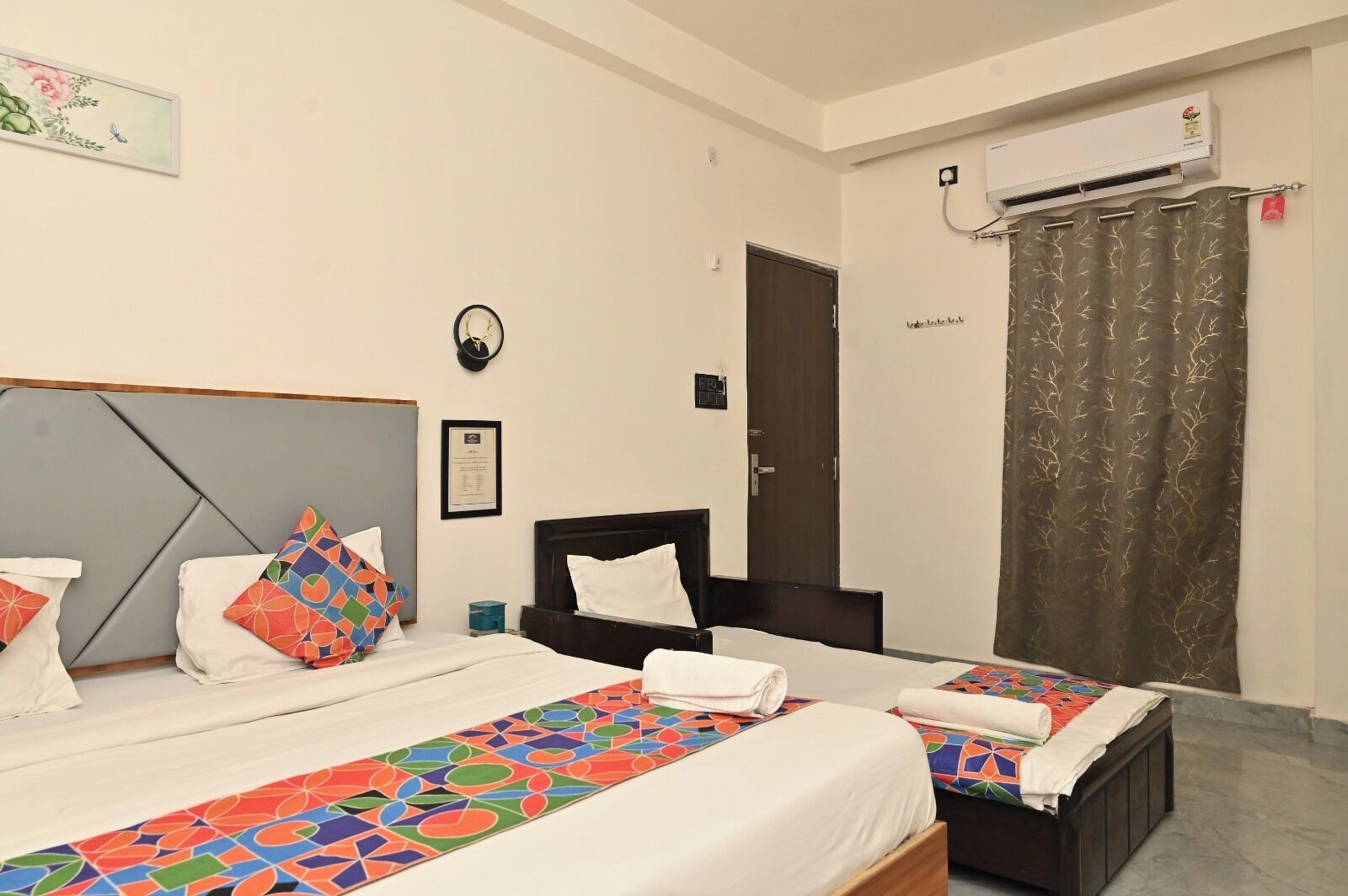 Habitación de hotel con dos camas, aire acondicionado de pared, una cortina y un certificado enmarcado en la pared.
