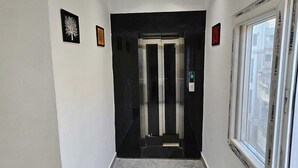 Een gang met een marmeren vloer, een lift en een raam met jaloezieën.