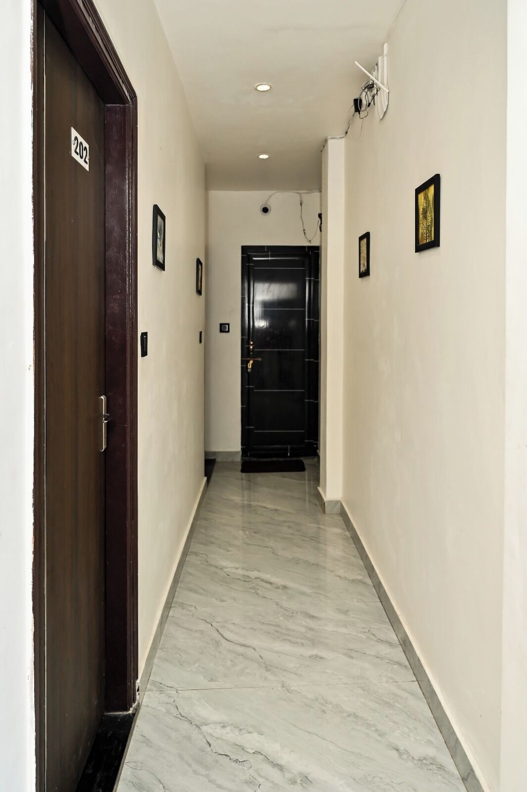 A hallway with a marble floor, a black door with a number sign, and a framed picture on the wall.