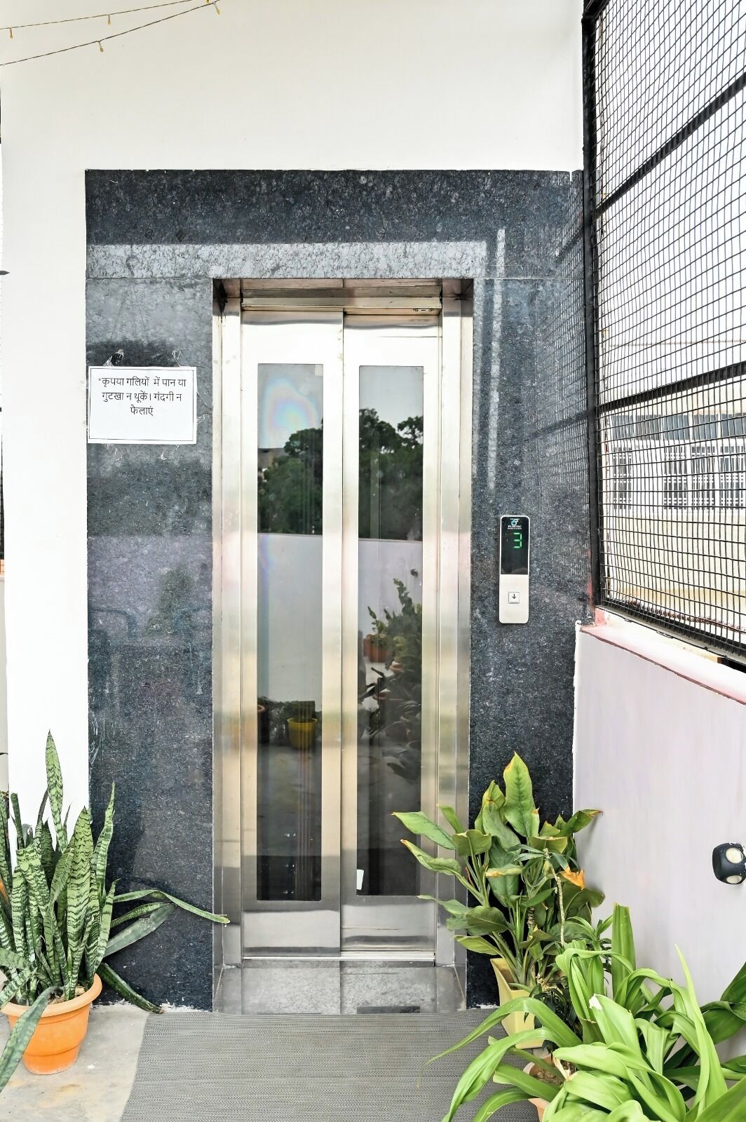 An elevator with a digital display, a sign in a foreign language, and potted plants.