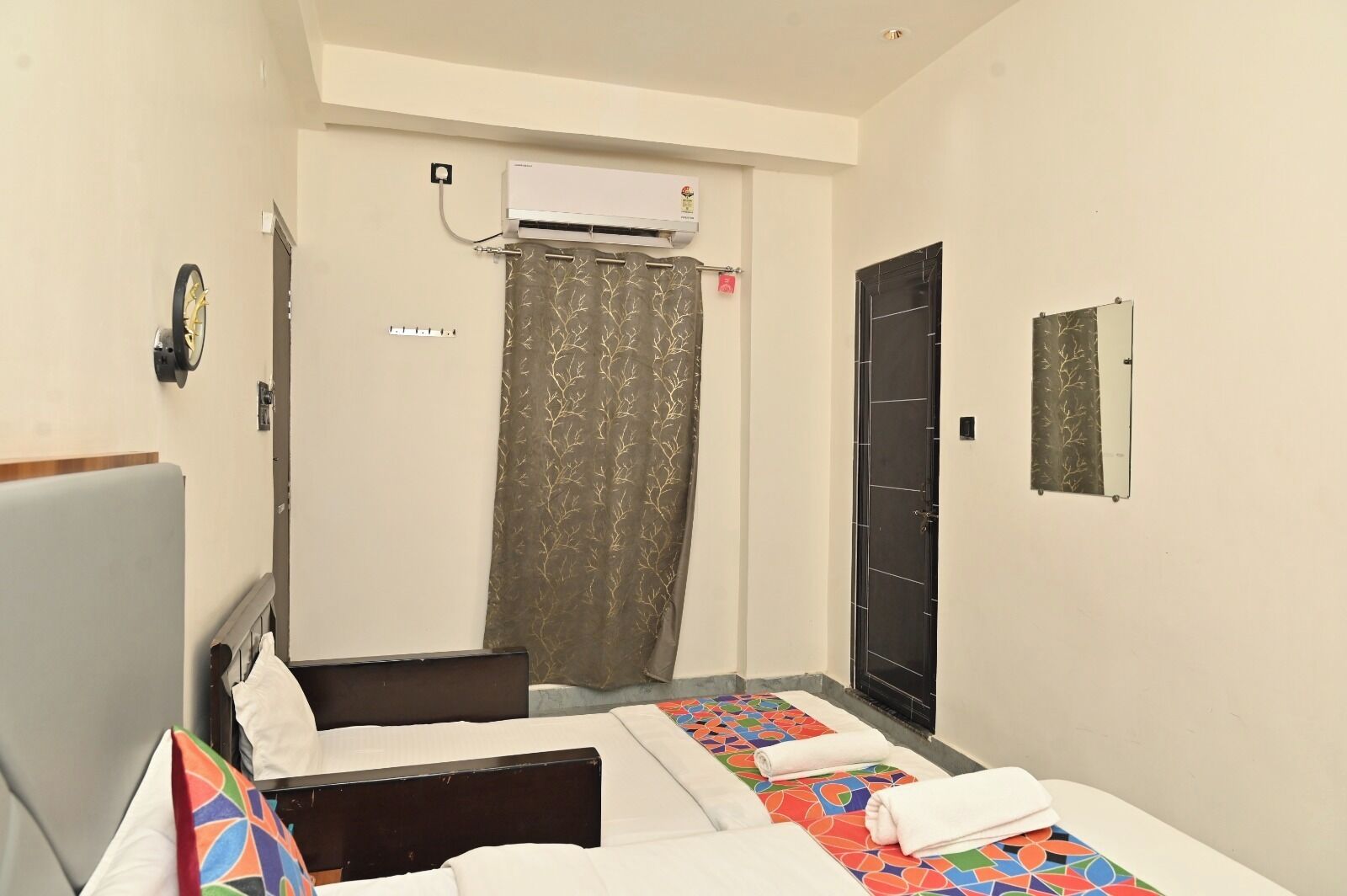 A hotel room with two beds, a shower, an air conditioning unit, and a door with a mirror.