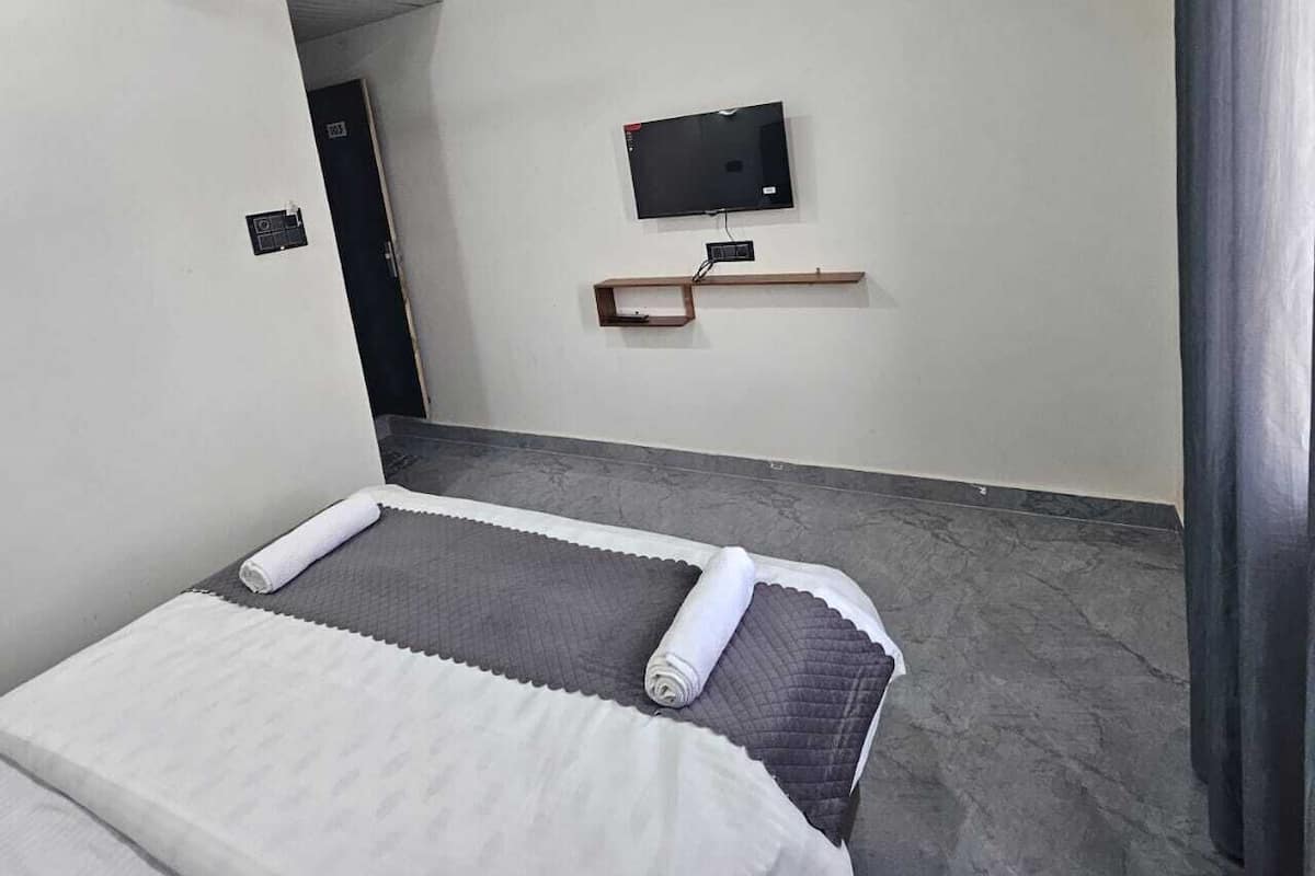 Una habitación de hotel con cama, ventilador de techo, televisor montado en la pared y una puerta que da a otra habitación.