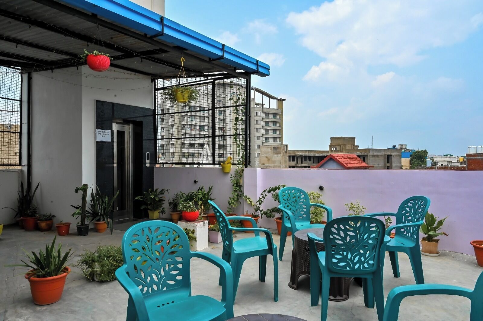 A rooftop terrace with potted plants, teal chairs, and a blue awning.