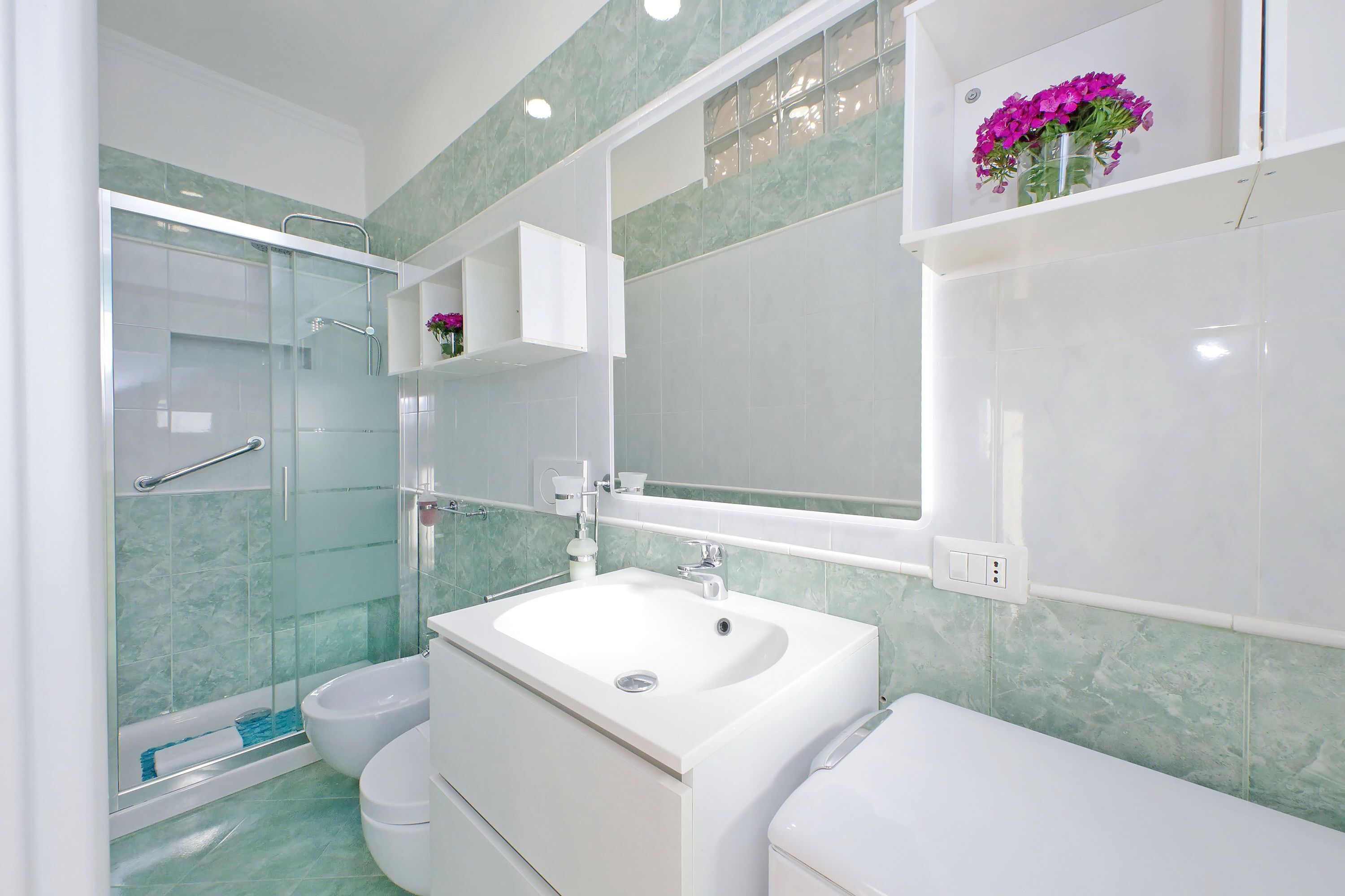 Ein modernes Badezimmer mit einer Glaskabine zur Dusche, einem weißen Waschbecken und einer Toilette.