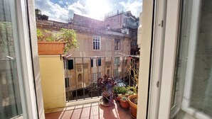Ein Balkon mit Blumentöpfen, Blick auf angrenzende Gebäude und einem Metallgeländer.