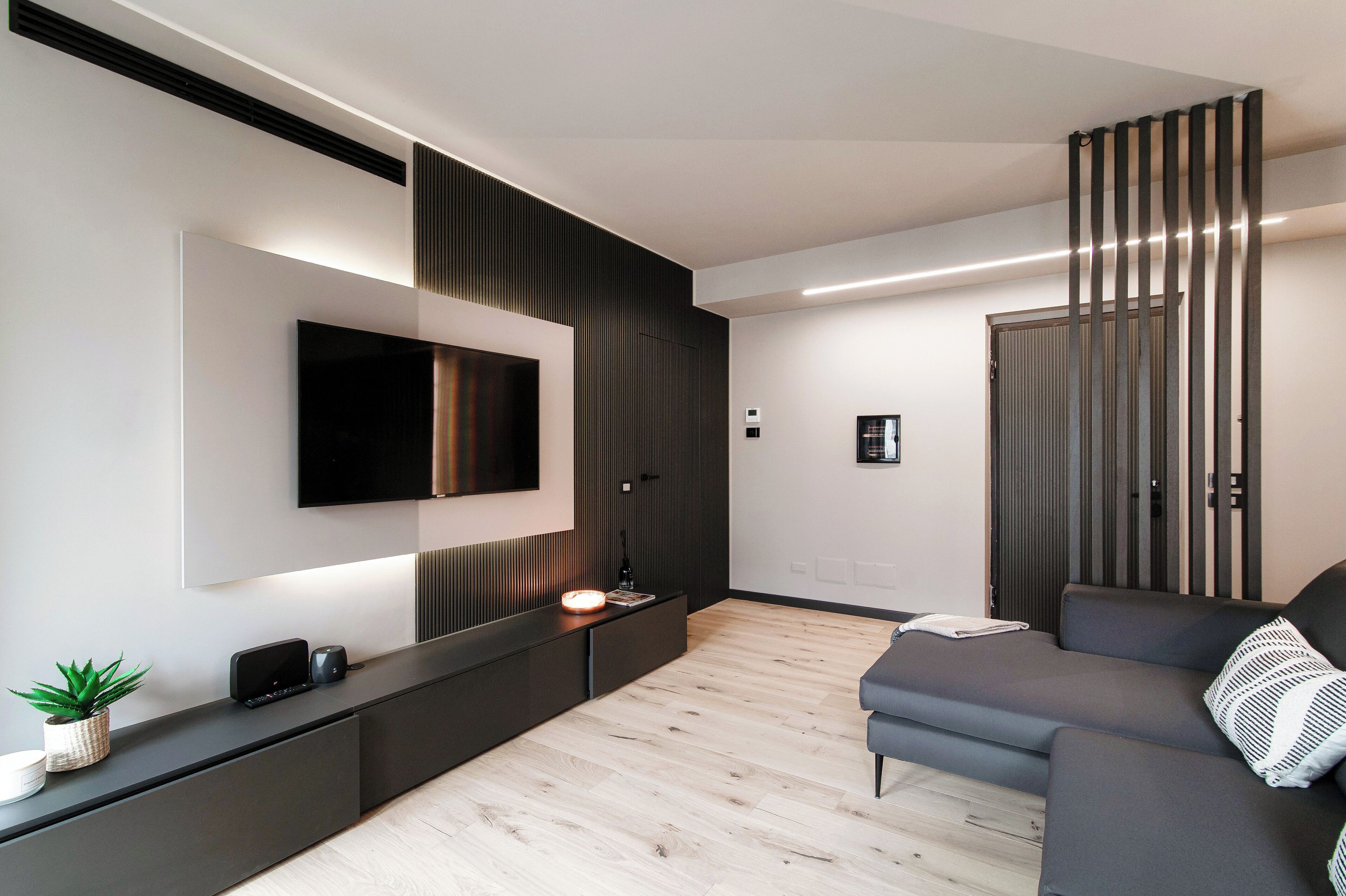 A modern living room with a flat-screen TV mounted on the wall, a dark-colored sofa, and a wooden floor.