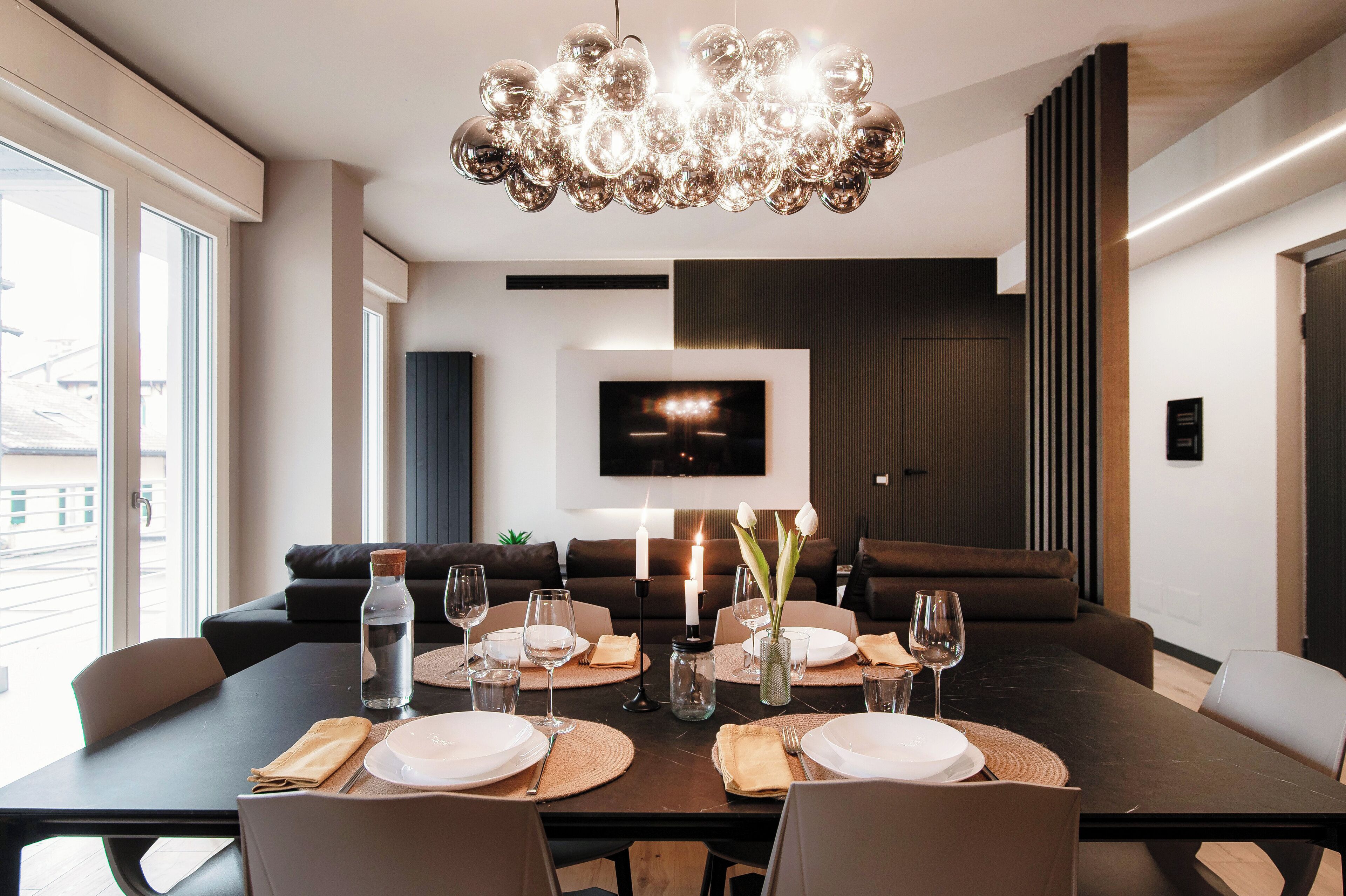 Un espace repas moderne avec une grande table dressée pour le repas, un lustre et un téléviseur à écran plat fixé au mur.
