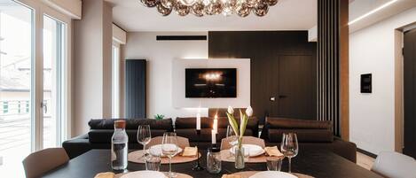 Un espace repas moderne avec une grande table dressée pour le repas, un lustre et un téléviseur à écran plat fixé au mur.