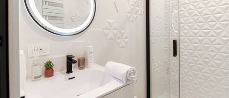 A modern bathroom with a round mirror, a sink, a towel, and a shower with geometric wall tiles.