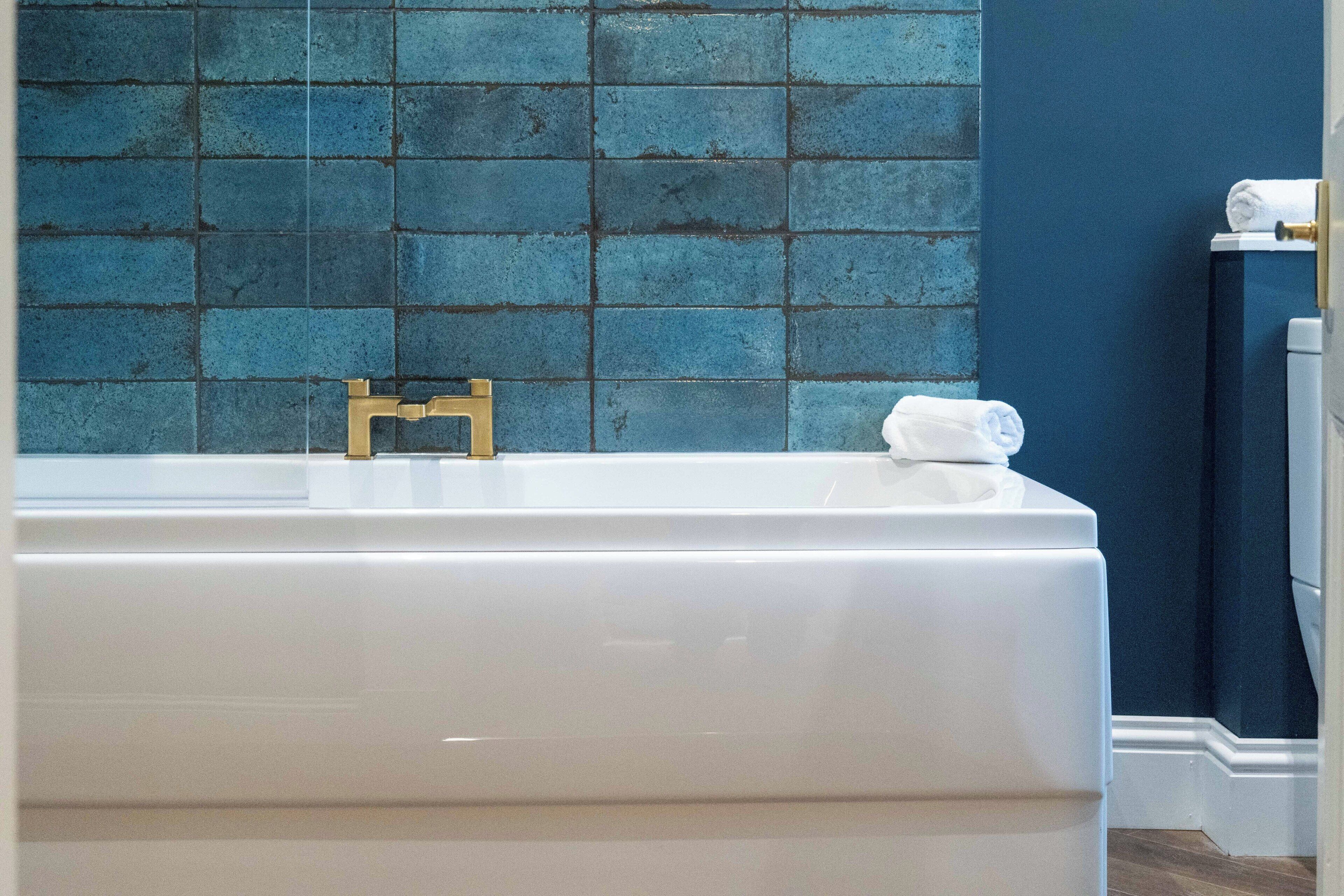 A bathroom with a white bathtub, a blue tiled wall, and a white towel on the side.