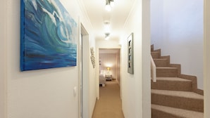 A hallway with a painting, a staircase, and a bed in the background.