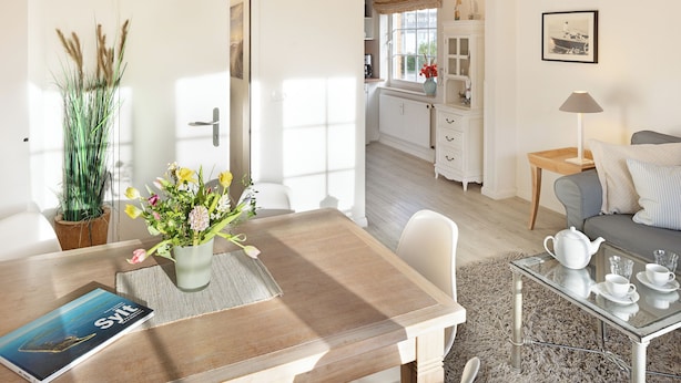 A well-lit room with a dining table, a sofa, and a kitchen area in the background.