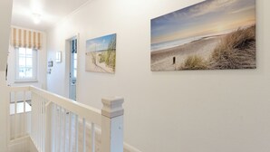 A hallway with white walls, a wooden railing, and three framed beach paintings.