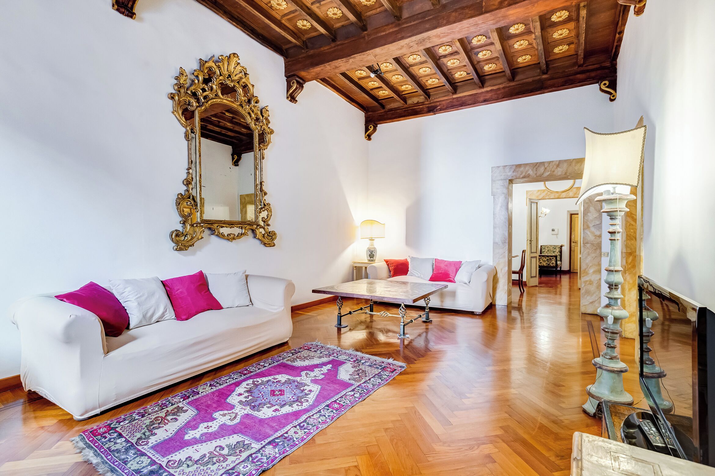 A spacious living room with a white sofa, a patterned rug, a wooden coffee table, and a decorative lamp.