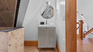 Une salle de bain avec un meuble-lavabo blanc, un miroir rond et un sol carrelé.