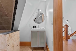 Un baño con tocador blanco, espejo redondo y piso de azulejos.