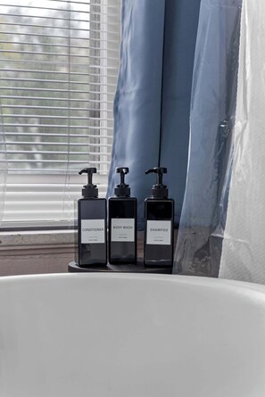 Three black bottles labeled conditioner, body wash, and shampoo on a white surface near a bathtub.