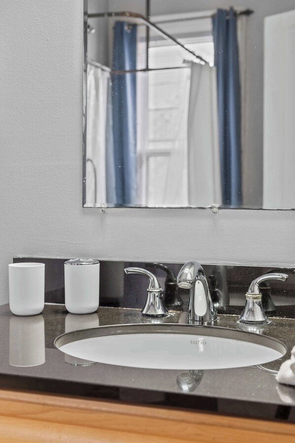Un baño con un lavamanos blanco, dos llaves y un espejo encima.