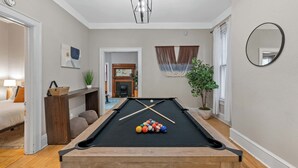 Ein Billardtisch mit Kugeln, eine hölzerne Bank, eine Pflanze und ein Spiegel an der Wand.