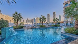 Un hôtel moderne doté d’une piscine, de palmiers et, en arrière-plan, de bâtiments de grande hauteur.