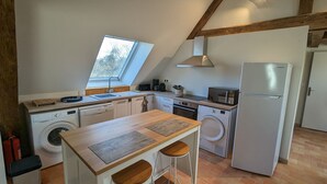 A compact kitchen with a washing machine, a microwave, a refrigerator, and a small dining area with stools. - Cottage in forest with garden, terrace and parking near Loire (Saint-Firmin-sur-Loire)
