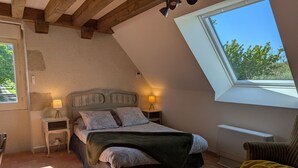 A bedroom with a sloped ceiling, a bed with a headboard, two bedside tables with lamps, a window with a view, and a chair. - Cottage in forest with garden, terrace and parking near Loire (Saint-Firmin-sur-Loire)