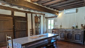 Un comedor rústico con una mesa de madera, un banco y sillas. Un armario grande de madera con cajones está contra la pared.