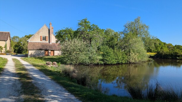 Una casa junto a un río tranquilo con un camino de grava que lleva a ella.