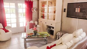 Una sala de estar con un sofá blanco, una mesa de centro de vidrio, un aparador blanco con puertas de vidrio y un televisor montado en la pared.