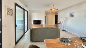 En moderne stue med en sofa, et træspisebord dækket til et måltid, og et fjernsyn i baggrunden.