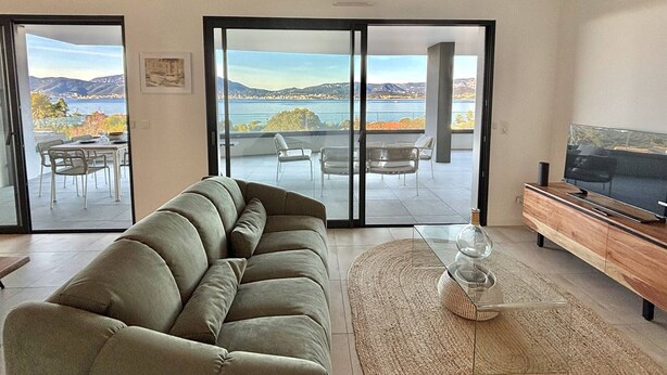 En moderne stue med sofa, fjernsyn og udsigt til en balkon med udendørs møbler.