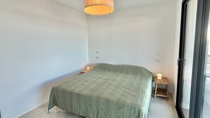 Et minimalistisk soveværelse med en seng, sengeborde med lamper og et stort vindue.