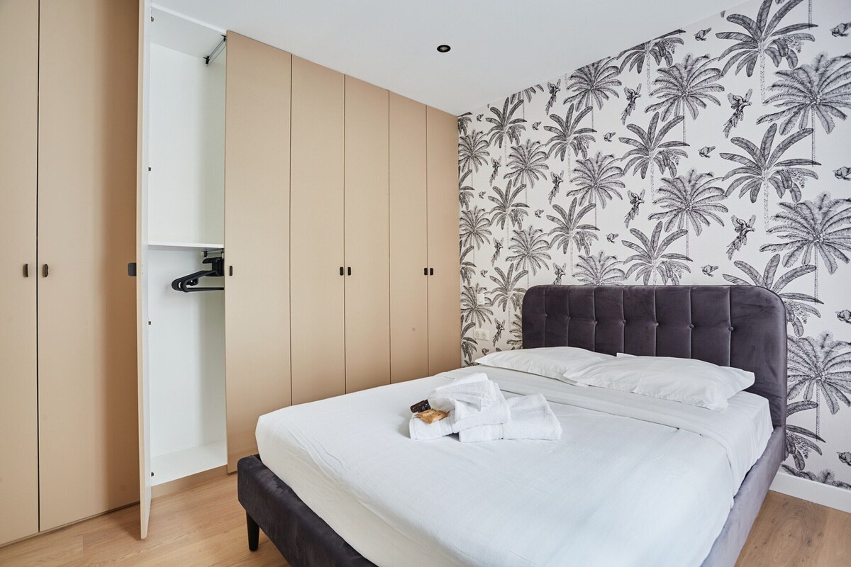 A bedroom with a bed, a wardrobe, and a wall with a tropical leaf pattern.