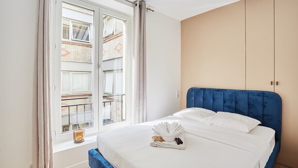 A bedroom with a bed, a window, and a view of a building outside. - Charming Duplex - Louvre Museum (Paris)