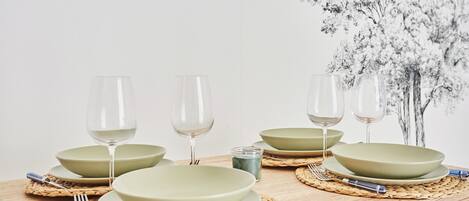 A dining table set with green plates, clear wine glasses, and silverware on woven placemats.