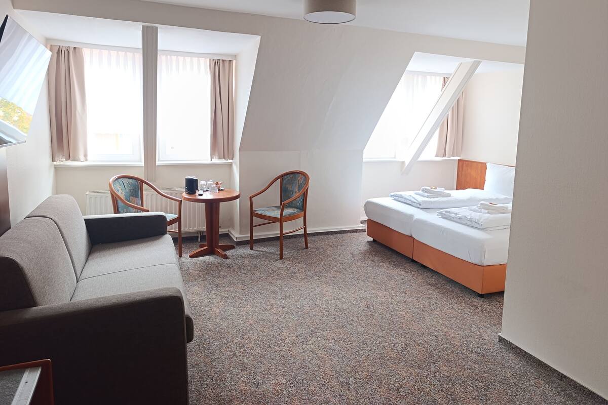 A hotel room with a bed, a sofa, two chairs, a small table, and a window with curtains.