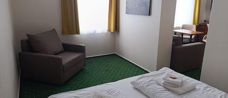 A hotel room with two beds, a sofa, a small table, and a painting on the wall.