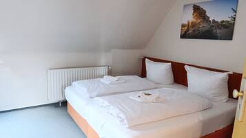 Ein Schlafzimmer mit schrägen Wänden, einem Heizkörper, einem Bett mit weißer Bettwäsche und einem Bild an der Wand.