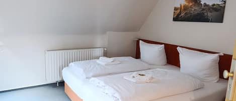 A bedroom with a sloped ceiling, a radiator, a bed with white linens, and a painting on the wall.