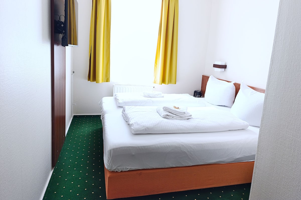 A hotel room with two beds, a green carpet, and yellow curtains.